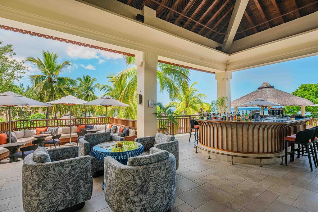Offener Bar- und Loungebereich im Hilton Mauritius Resort & Spa mit floralen Sesseln, Holztresen und Palmen im Hintergrund