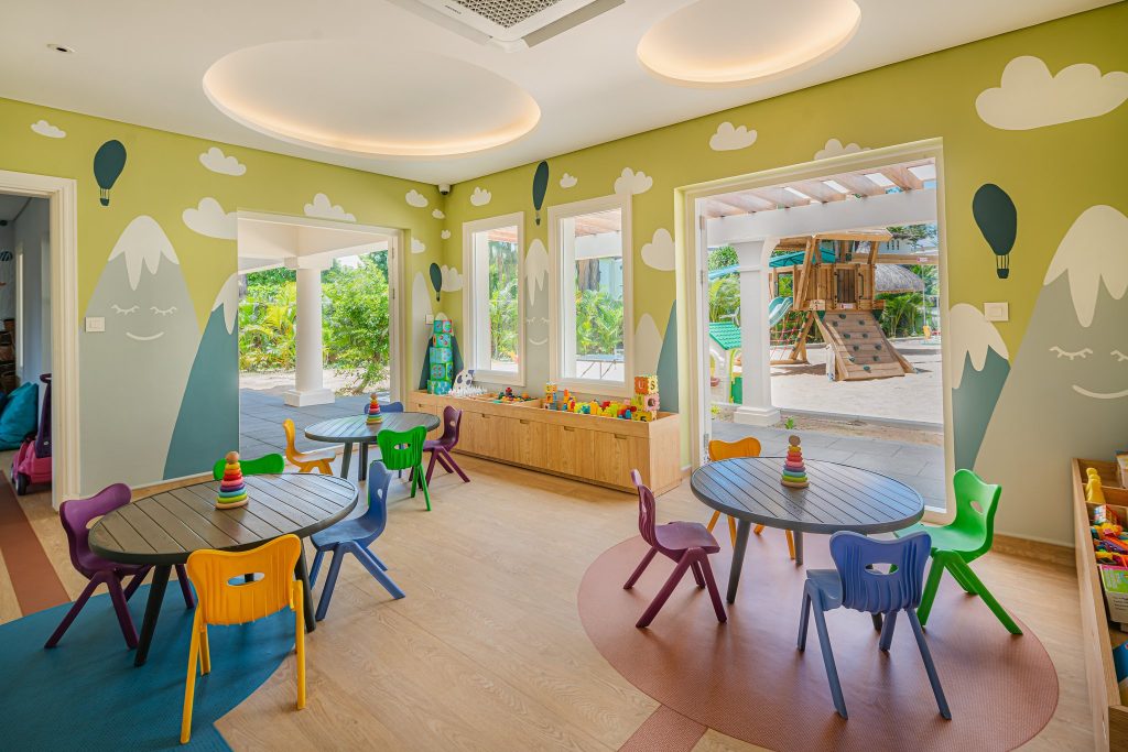 Kinderbereich mit ovalen Holztischen, bunten Stühlen und kindgerechten Wandmalereien im Hilton Mauritius Resort & Spa