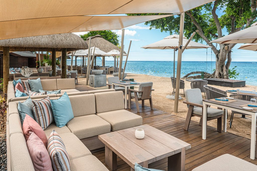 Hotelterrasse des Restaurants Coquillages mit stoffbezogenen Sofas, Holzmöbeln und Sonnensegeln direkt am Strand