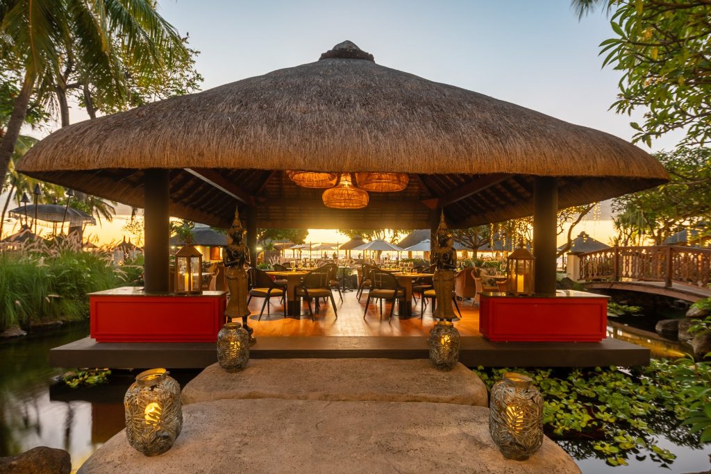 Offenes Restaurant Ginger Thai mit Holzfußboden, Strohdach, Wasserflächen und zwei dekorativen Statuen am Eingang
