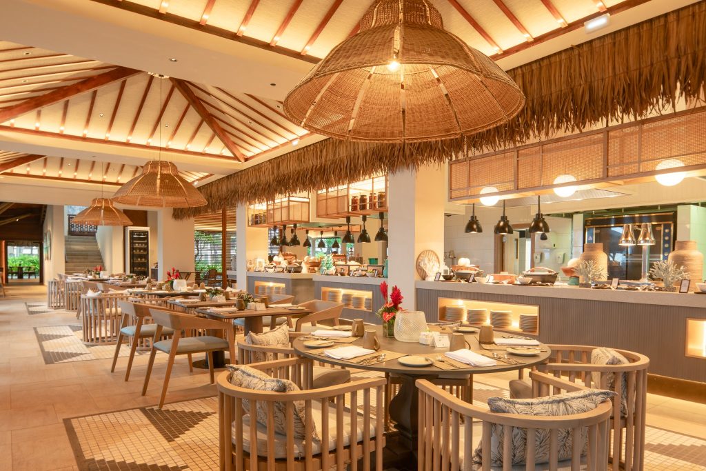 Restaurant Pomme d'Amour mit Holztischen, Korbleuchten, Holzbalkendecke und grünen Pflanzen