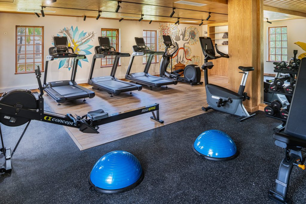 Fitnessraum im Hilton Mauritius Resort & Spa mit Laufbändern, Rudergerät, Holzboden und farbigen Wandmalereien