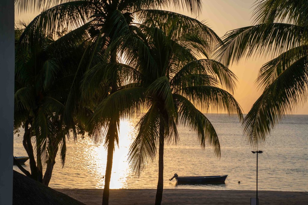 Strand mit Palmen und kleinem Boot auf ruhigem Wasser bei Sonnenuntergang im Hilton Mauritius Resort & Spa