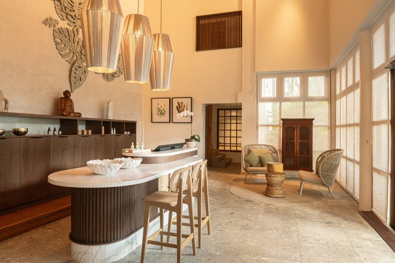 Hotel-Lobby mit dunklem Holzempfang, hellem Marmor, metallischen Lampen und einer Buddha-Statue am Regal