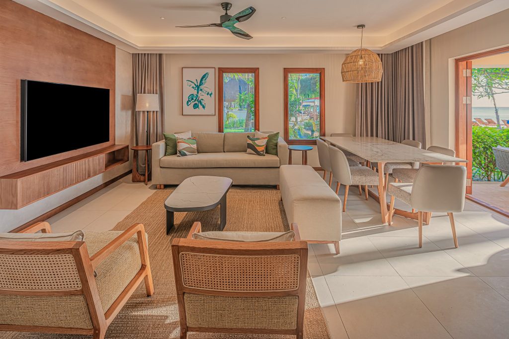 Moderner Wohnraum der Beach Front Family Suite mit Sofa, Holzsesseln, großen Fenstern und tropischem Ausblick
