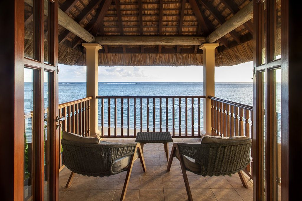 Überdachte Terrasse der Beach Front Junior Suite mit zwei geflochtenen Stühlen, kleinem Holztisch und Meerblick