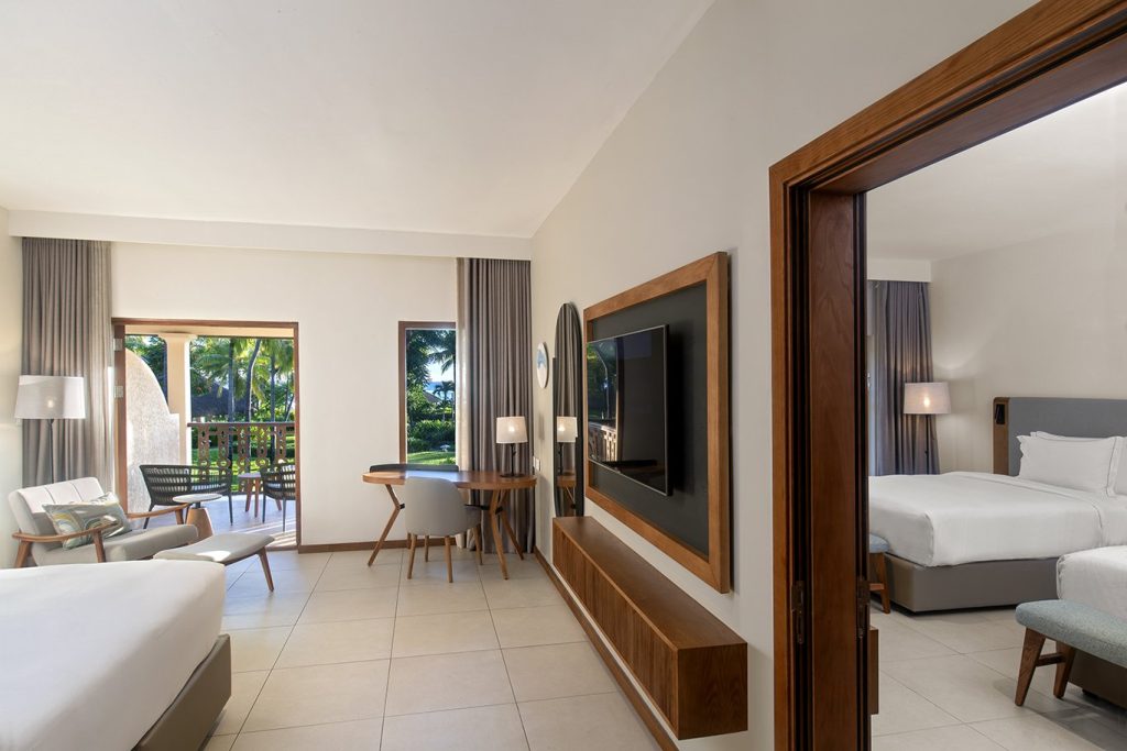 Modernes Connecting Deluxe Room Zimmer im Hilton Mauritius Resort & Spa mit Holzsitzgruppe und Blick auf grüne Außenanlage
