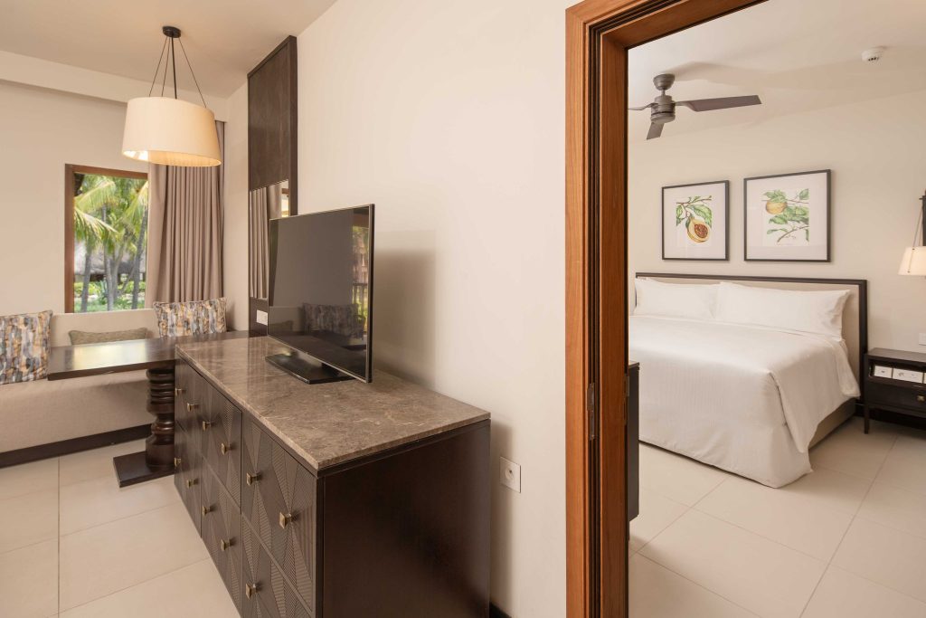 Wohnzimmer und Schlafzimmer des connecting-grand-deluxe-room im Hilton Mauritius Resort & Spa mit Marmorkommode.