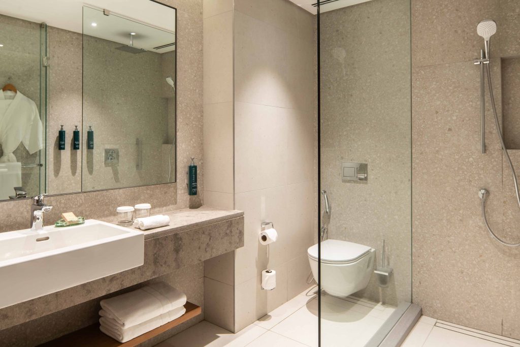 Modernes Badezimmer im Hilton Mauritius Resort & Spa King Deluxe Room mit beigen Fliesen, großer Spiegel.