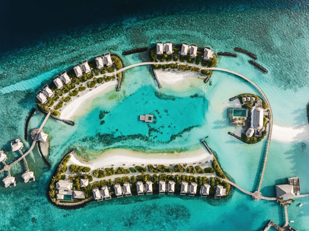 Luftaufnahme mehrerer über Wasser stehender Bungalows mit Holzstegen und klarem Wasser auf den