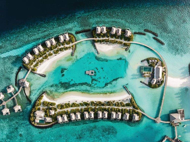Luftaufnahme mehrerer über Wasser stehender Bungalows mit Holzstegen und klarem Wasser auf den