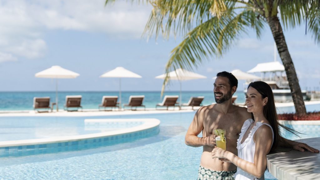 Paar an der Poolbar des InterContinental Maldives Maamunagau Resort mit Sonnenschirmen, Liegestühlen und Blick auf das Meer