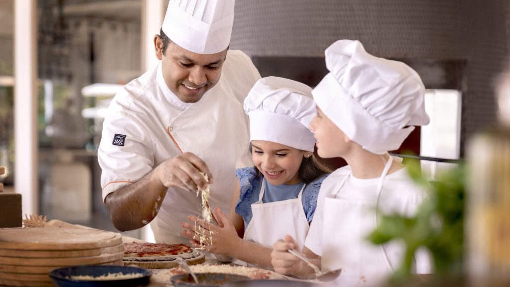 Koch und zwei Kinder in der Hotelküche des InterContinental Maldives Maamunagau Resort bei Kochunterricht