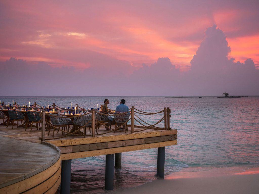Terrasse des Restaurant Lighthouse mit Holztischen und Stühlen aus Naturmaterialien bei Sonnenuntergang auf den