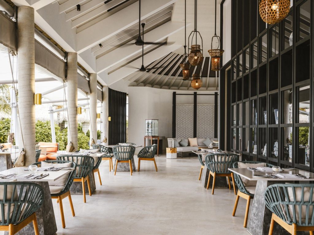 Restaurantbereich im InterContinental Maldives Maamunagau Resort mit Holzmöbeln, weißen Tischen und geflochtenen Lampen