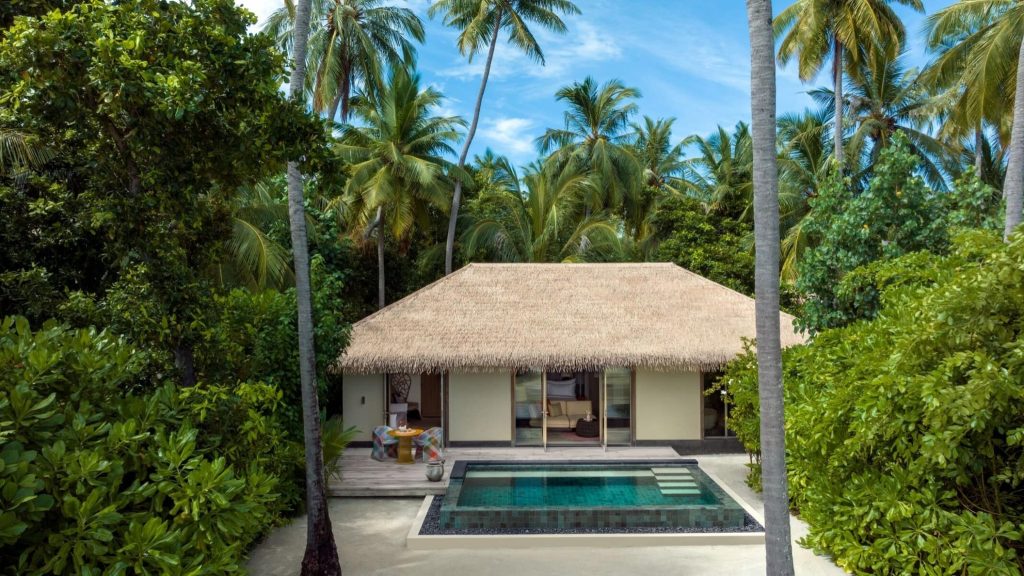 Bungalow mit strohgedecktem Dach, großen Glasschiebetüren, kleinem Pool und tropischer Vegetation auf den