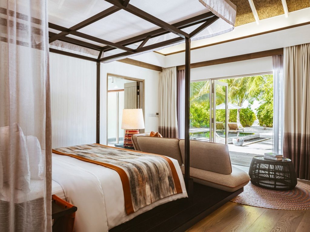 Hotelzimmer mit Himmelbett, gepolsterter Sitzgelegenheit, Couchtisch, buntem Teppich und Blick auf Pool