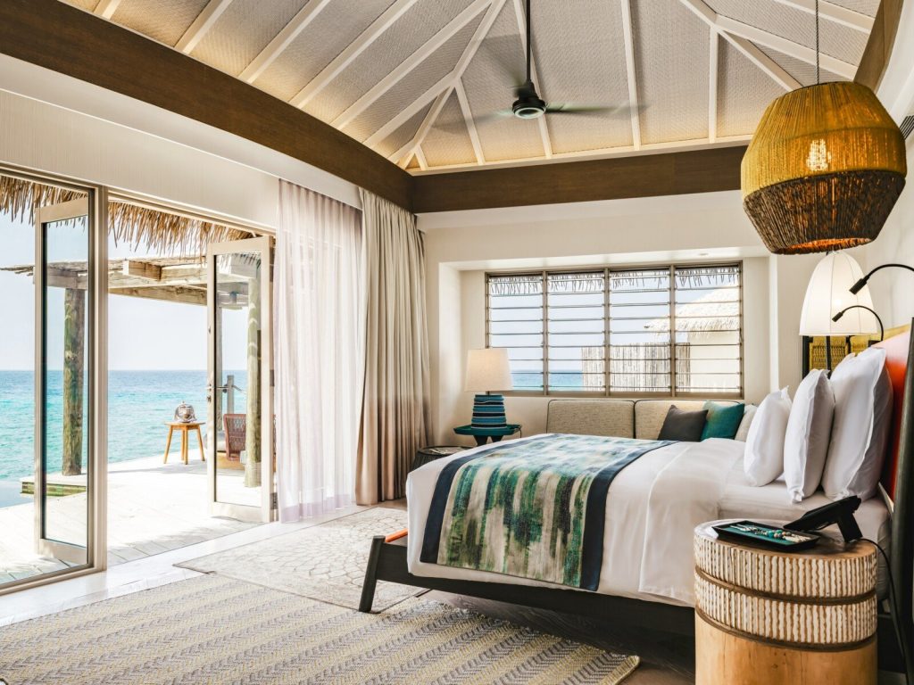 Zimmer im InterContinental Maldives Maamunagau Resort mit großem Bett, blau-grünem Überwurf und Meerblick durch