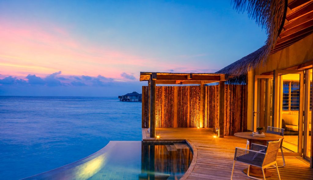 Terrasse einer Overwater Pool Villa mit Holzboden, privatem Pool und Sicht auf das Meer bei Sonnenuntergang