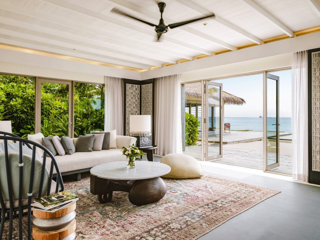 Wohnbereich der Three Bedroom Lagoon Residence mit großem Fenster, Terrasse und Meerblick im InterContinental Maldives.