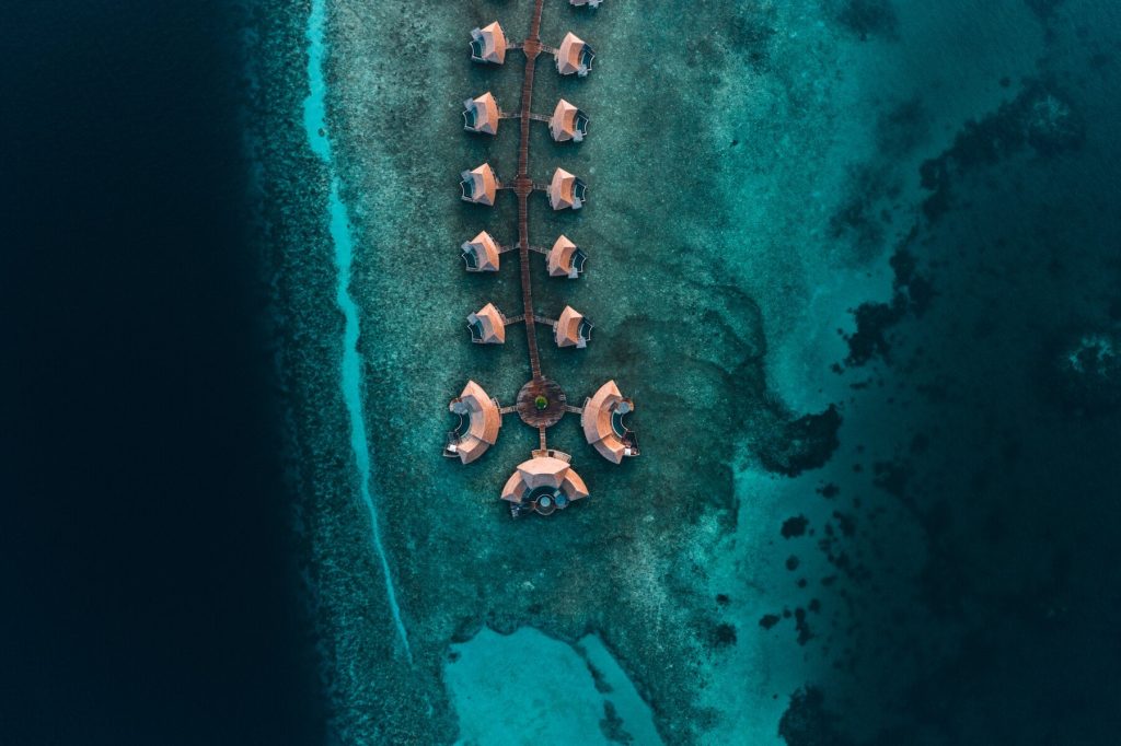 Luftaufnahme der Three Bedroom Overwater Residence mit runden Holzbungalows auf Steg über türkisfarbenem Meer in den.