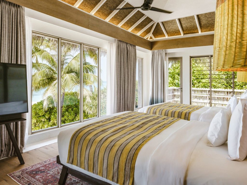 Modernes Hotelzimmer mit zwei Betten, gelb gestreiften Tagesdecken und Meerblick auf den