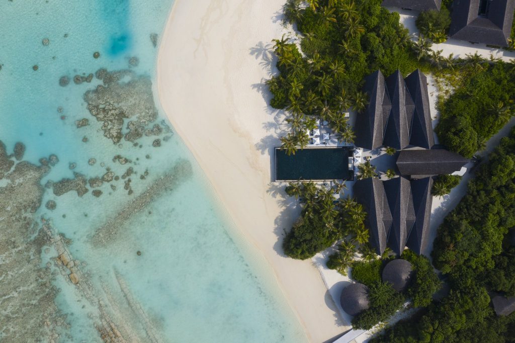 Luftaufnahme des Kuredhivaru Resort and Spa Maldives mit Sandstrand, rechteckigem Pool und mehreren Gebäuden mit dunklen.