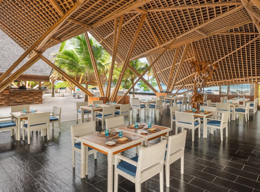 Offenes Restaurant Bar Latitude mit Bambusdach, hellen Holzmöbeln und Blick auf Palmen und Meer in den