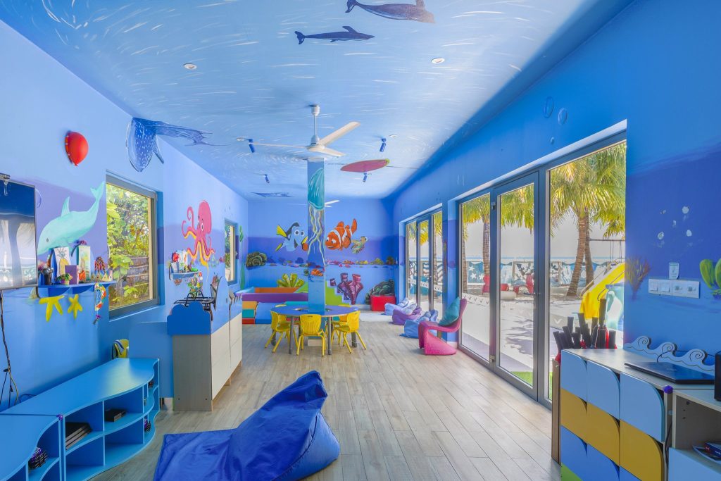 Kinderfreundlicher Raum im Kuredhivaru Resort and Spa Maldives mit maritimen Wandmalereien, bunten Möbeln und großen Fenstern