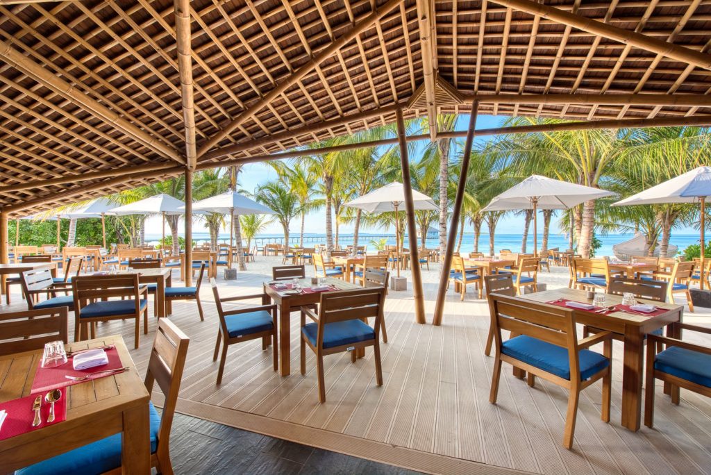 Offenes Strandrestaurant Onu Marche im Kuredhivaru Resort mit Holzdach, blauen Sitzpolstern und Palmen im Hintergrund