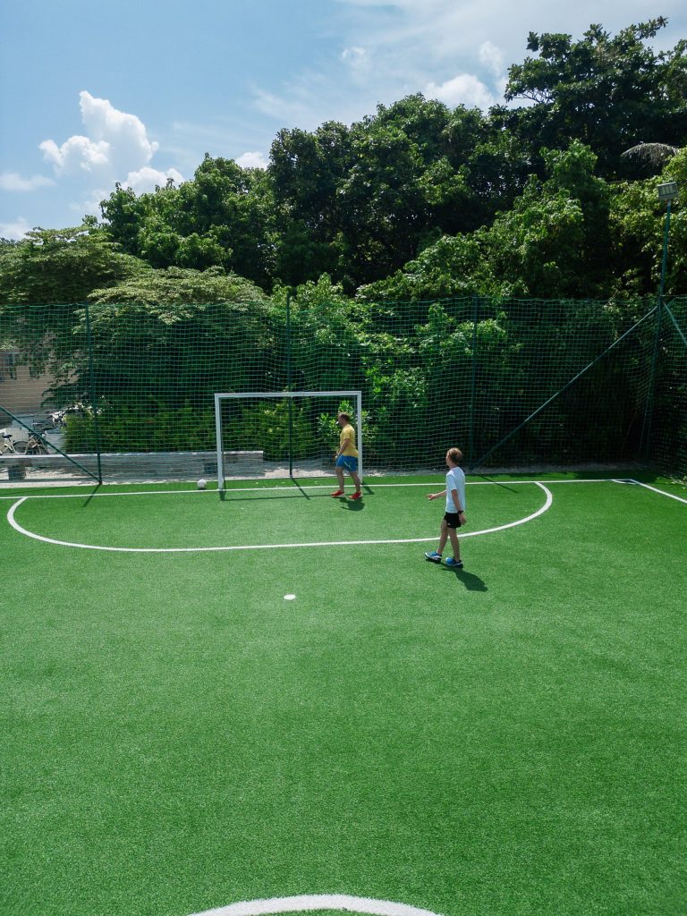 Kleiner Fußballplatz mit leuchtend grünem Kunstrasen, umgeben von grünem Zaun und Bäumen im Kuredhivaru Resort Maldives