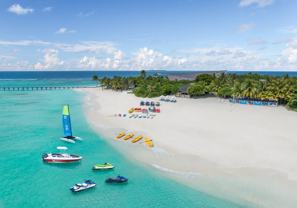 Strandabschnitt mit weißem Sand, türkisfarbenem Wasser, Kanus, Jetskis und Katamaran am Ufer im Kuredhivaru Resort Maldives