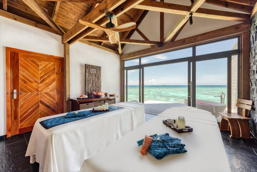 Heller Wellness Spa Raum mit zwei Massagebänken, Holzdecke, Natursteinwänden und Meerblick durch Glastür