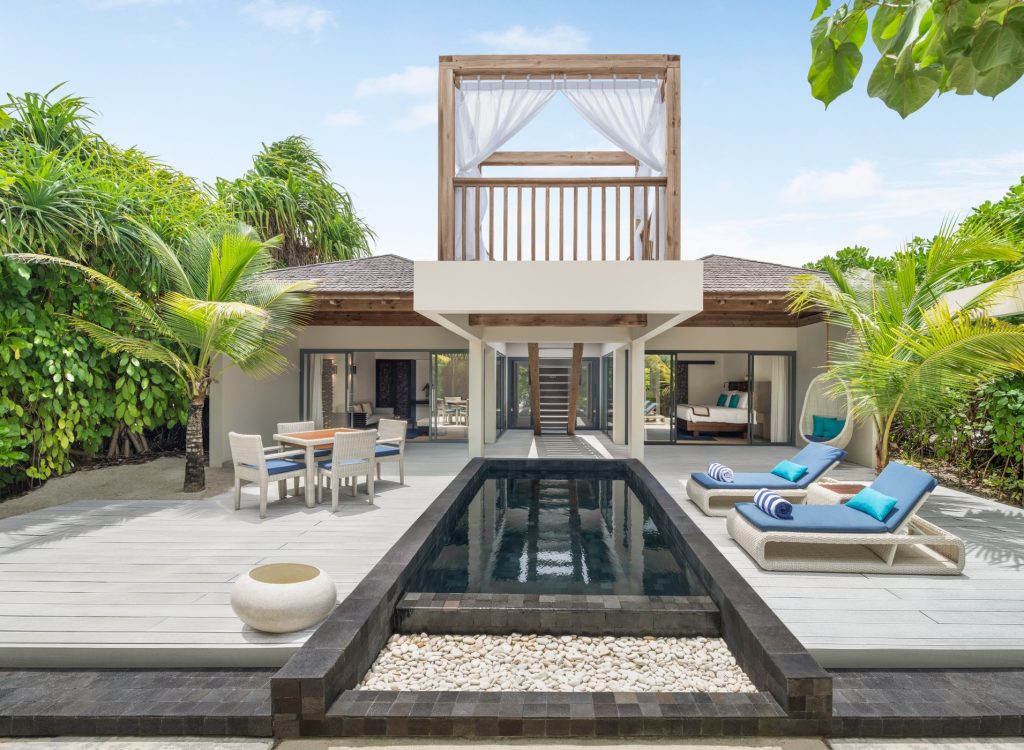 Moderne Beach Pool Villa mit zentralem Pool, Holzterrasse, blauen Liegen und Esstisch im Kuredhivaru Resort Maldives
