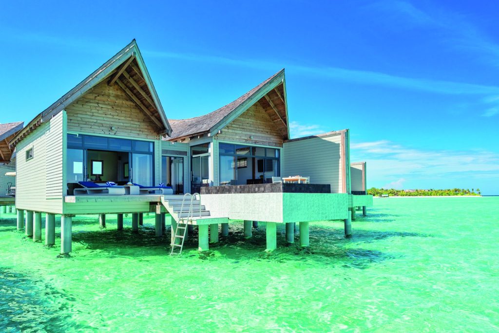 Über dem Wasser gebautes Holzhaus mit Satteldach, großen Glasfenstern und Treppe ins türkisblaue Wasser