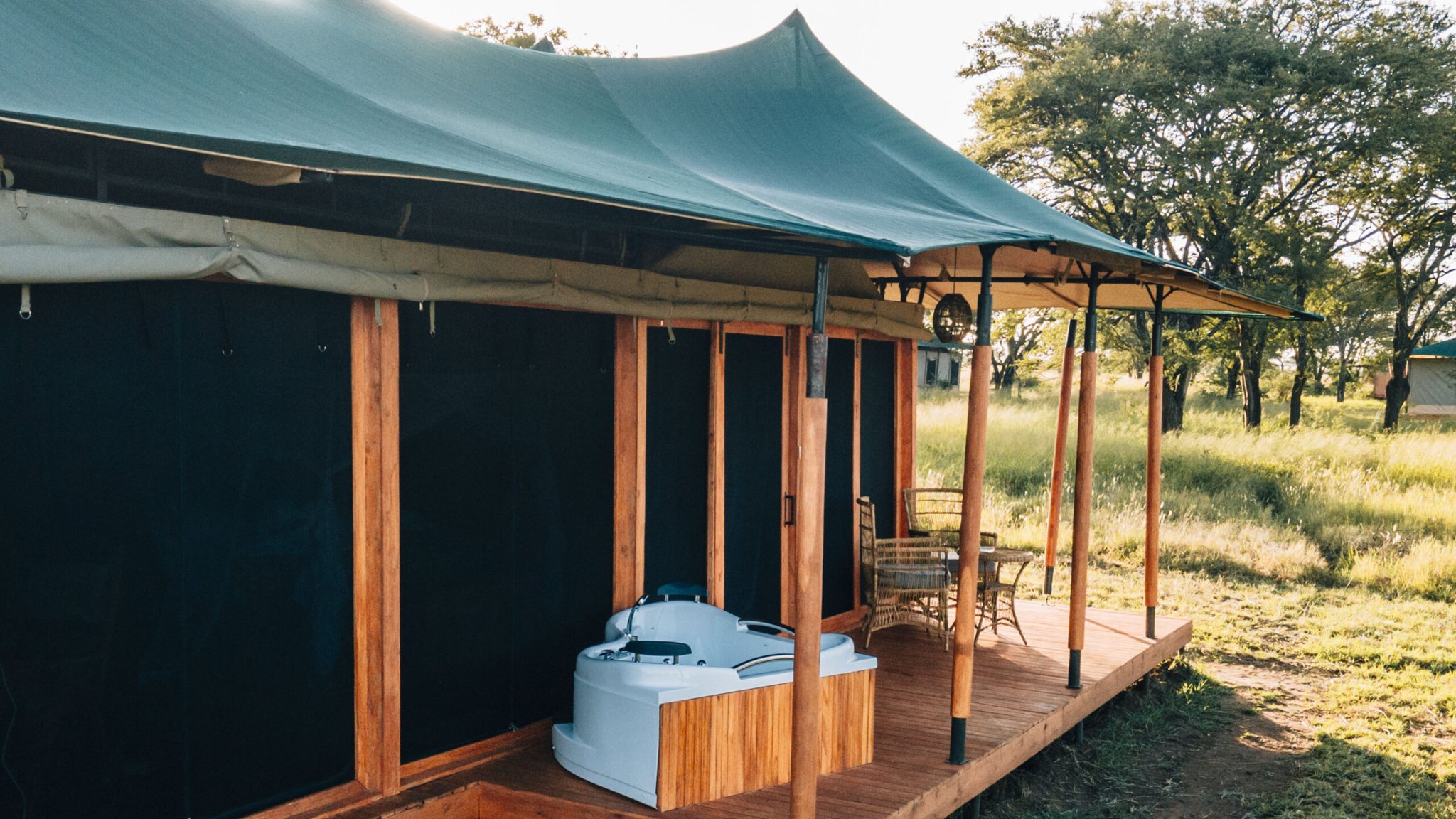 Misako Mara Migration Camp Safari-Zelt mit Whirlpool Safari-Zelt mit dunkelgrünem Stoff auf Holzterrasse, Whirlpool und Gartenmöbel aus geflochtenem Material