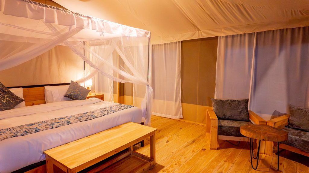 Hotelzimmer im Misako Ndutu Migration Camp mit großem Baldachinbett, Holzmöbeln und warmem Licht in Tansania