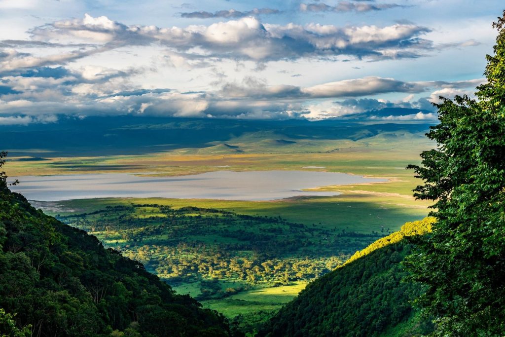 Ngorongoro Lions Paw Panorama mit Gartenblick Weite Landschaft mit See in der Bildmitte, grünen Hängen im Vordergrund und bewölktem Himmel in Tansania