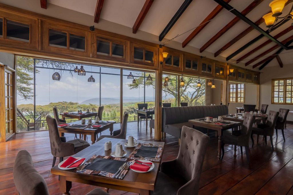 Innenraum des Ngorongoro Lions Paw Restaurants mit großen Glasfenstern und Blick auf grüne Landschaft in Tansania