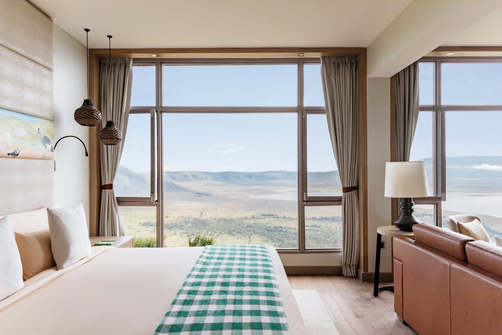 Modern eingerichtetes Hotelzimmer mit großem Panoramafenster, Bett mit weißer Bettwäsche und grün-kariertem Überwurf.