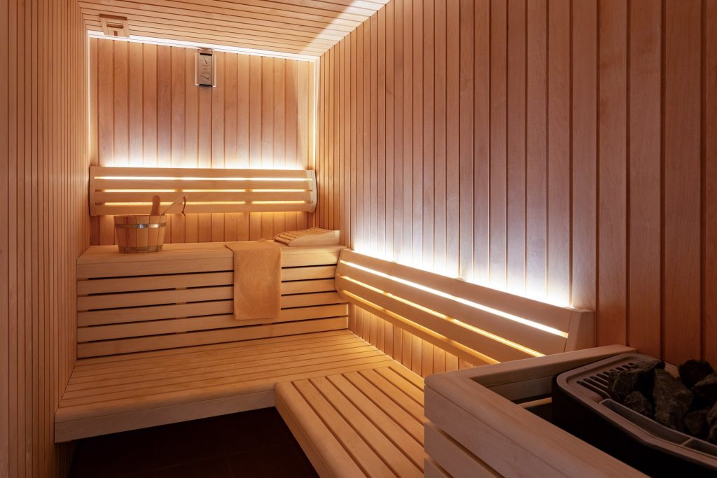 Sauna mit hellen Holzwänden, Bänken und Saunaofen mit Steinen in Ngorongoro Lodge Meliá Collection