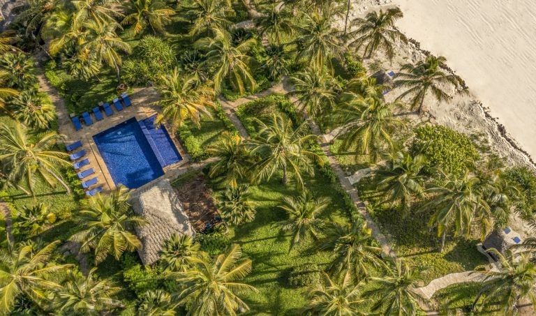 Draufsicht auf The Palms Zanzibar Pool mit dunkelblauem Wasser, blauen Liegestühlen und Palmen umgeben