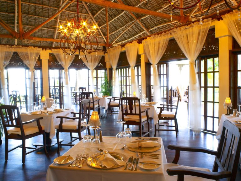 Restaurantbereich im The Palms Zanzibar mit dunklem Holzfußboden, Bambusdecke und bodentiefen Glastüren
