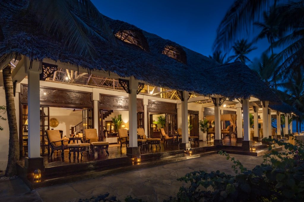 Außenansicht des The Palms Zanzibar Restaurants mit Holzterrasse, Schilfdach und geschnitzten Holzsäulen bei Dämmerung