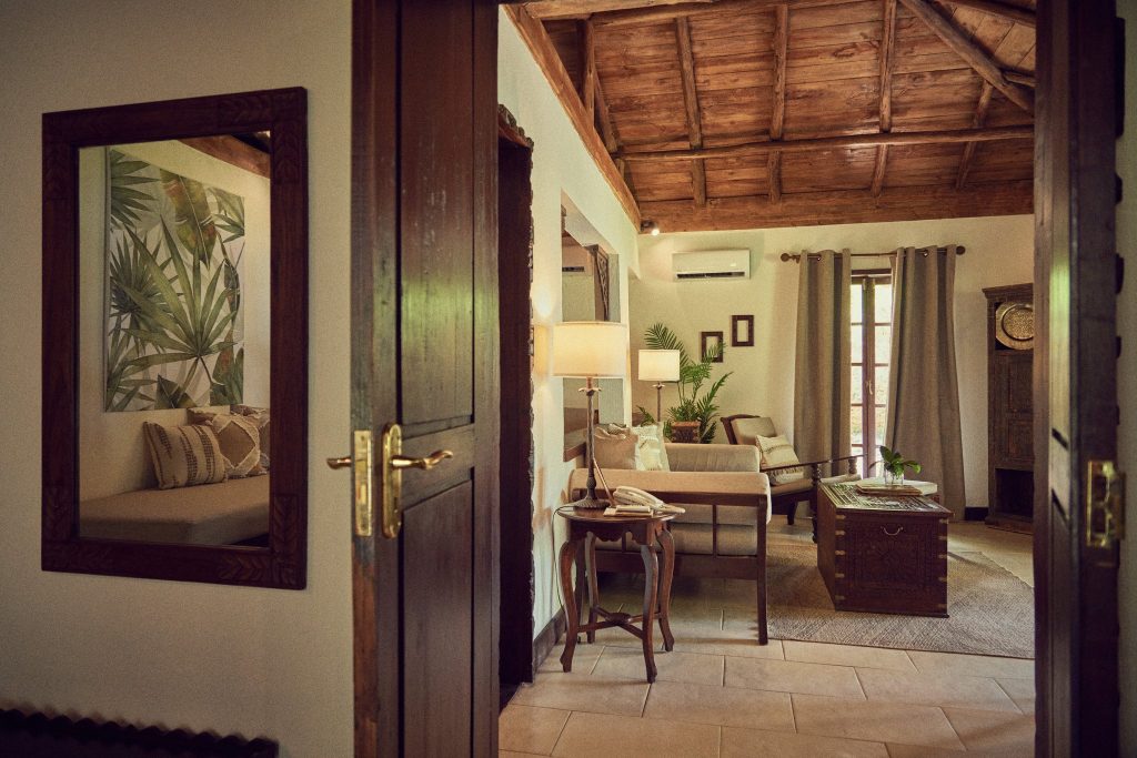 Hotelzimmer in The Palms Zanzibar mit Holzmöbeln, Holzdecke, großen Fenstern und beigefarbenen Vorhängen