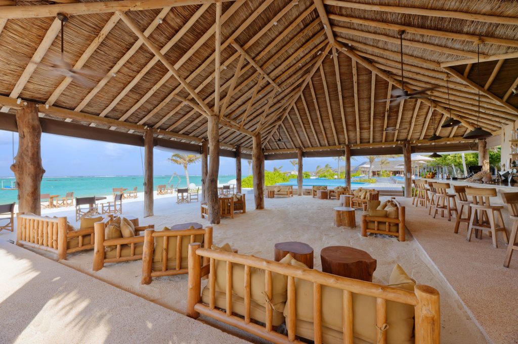 Offene Strandbar You & Me Maldives Cheers Bar mit Holzdach, Holzmöbeln und Blick auf das türkisfarbene Meer