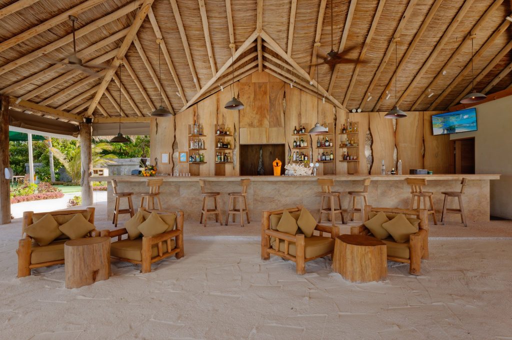 Offene Cheers Bar im You & Me Maldives mit hellen Holzmöbeln, Strohdach, Sandboden und tropischen Pflanzen
