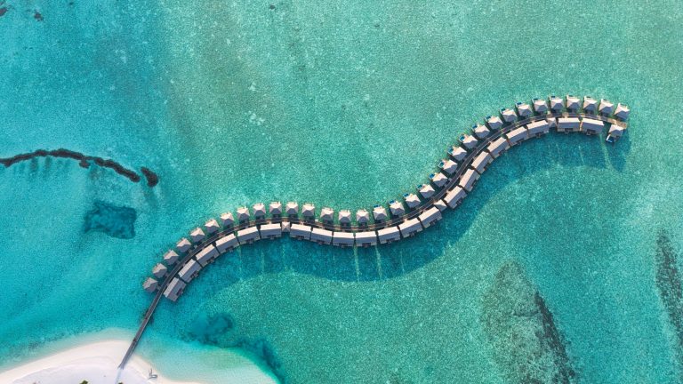 Luftaufnahme des You & Me Maldives Resortes mit Holzbungalows auf Stelzen über türkisfarbenem Meer