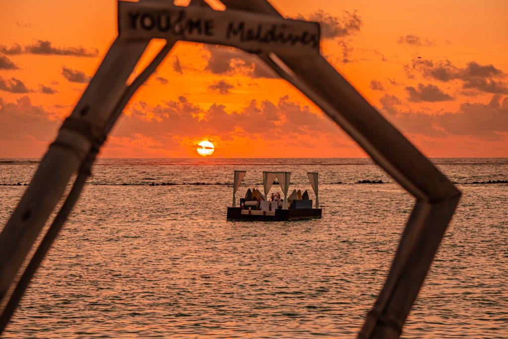 Schwimmender Steg mit überdachtem Essbereich bei Sonnenuntergang auf den Malediven, Holzkonstruktion mit Schriftzug