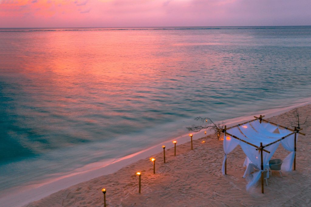 Strandabschnitt mit Bambuspavillon, Holzfackeln und Meer bei Sonnenuntergang auf den